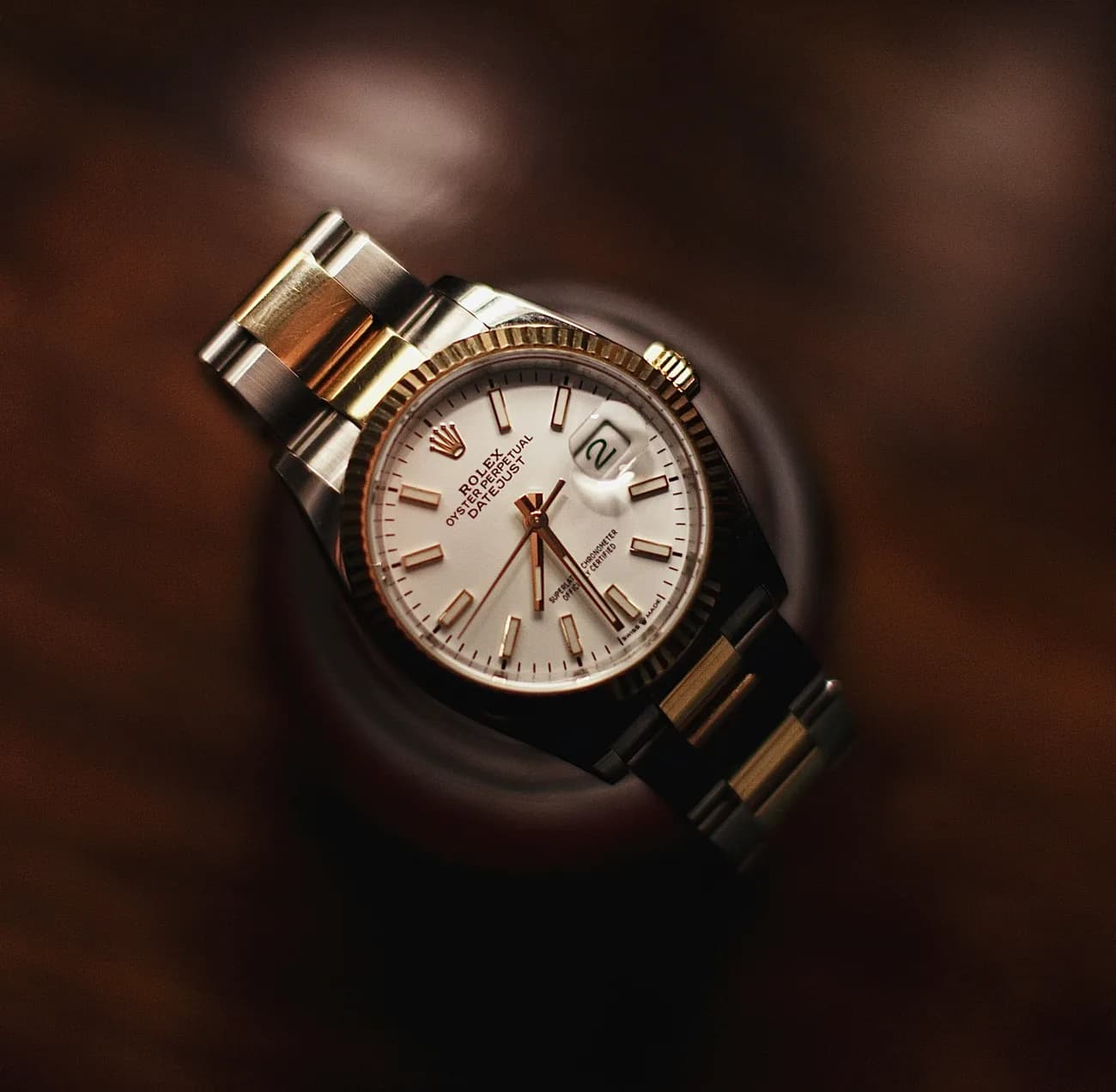 A gold and steel wristwatch resting on a dark wooden surface
