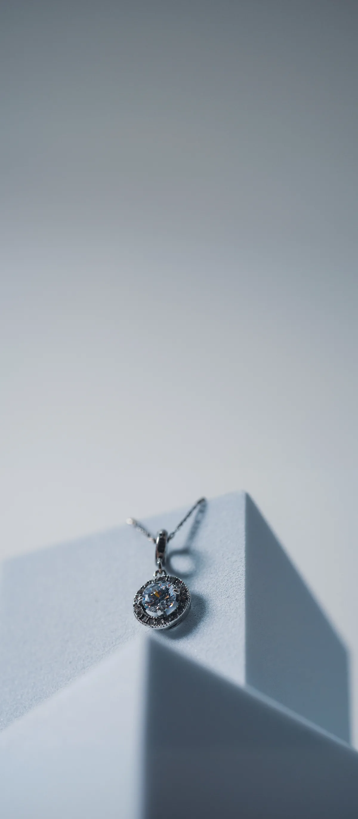 A diamond pendant necklace resting on a pale display plinth